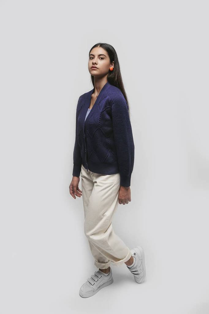 femme brune debout avec une veste bleu marine et un pantalon blanc