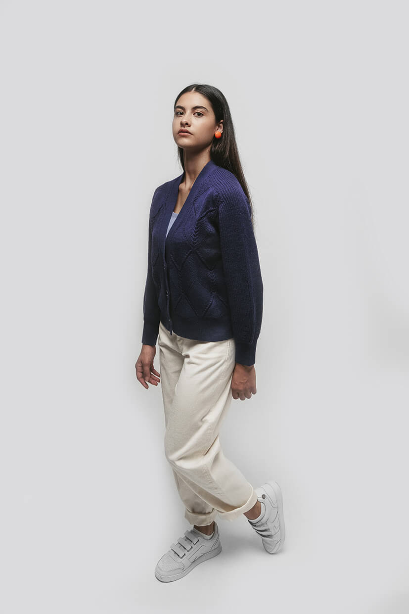femme brune debout avec une veste bleu marine et un pantalon blanc